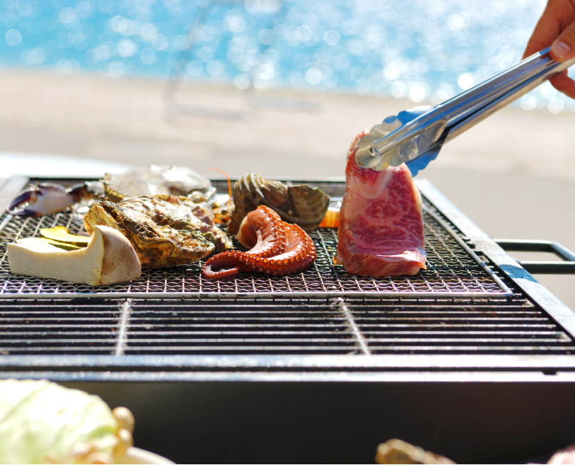 写真：きのこやお肉、タコや牡蠣など海鮮を焼いてお召し上がりいただける海辺でのバーベキューとオレンジ色の夕日