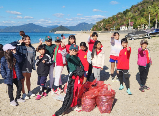 写真：海岸で集めたゴミを袋にまとめ、ピースをして記念写真を撮っている子どもたち