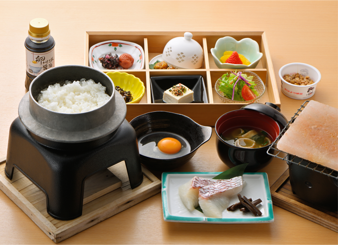写真：釜炊きの白いご飯、生卵、納豆、焼いて食べるお魚やサラダ、お味噌汁などセットになった朝食
