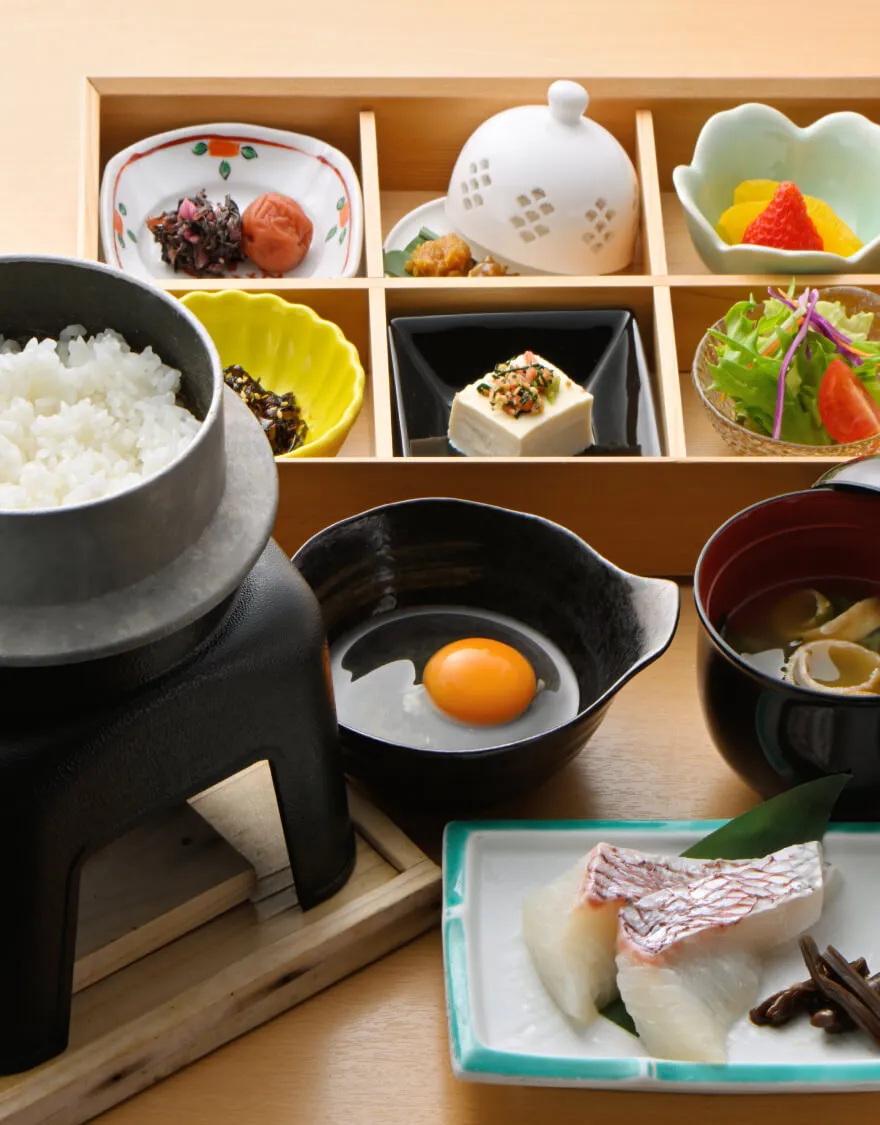 写真：お釜で炊いたご飯と生卵、お刺身など様々なおかずのついた朝食