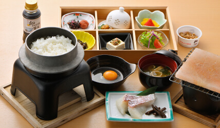 写真：お釜で炊いたご飯と生卵、お刺身など様々なおかずのついた朝食