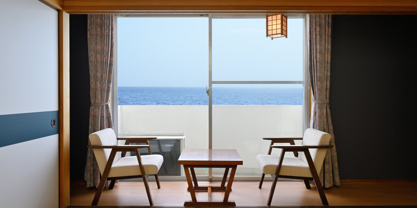 写真：海が見える窓側に椅子2台と机が設置された和室8畳の客室